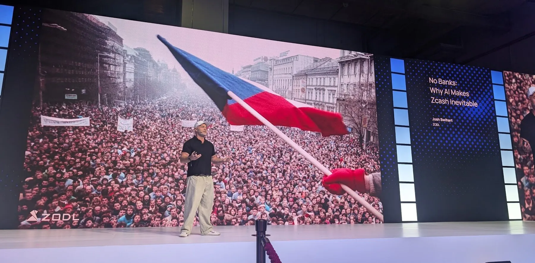 Josh Swihart on stage at TOKEN2049 Singapore in front of a photo of a 1989 Prague crowd with a Czech flag, next to his title slide 'No Banks: Why AI Makes Zcash Inevitable'